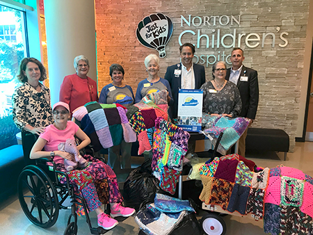 Marlene McComas, Dottie Crouch, and Jenn Williams were joined by Amy Lynn and Michelle Lawson to present the blankets to Norton Children's Hospital Medical Director Mark McDonald MD and Rev. Robin Hogle.