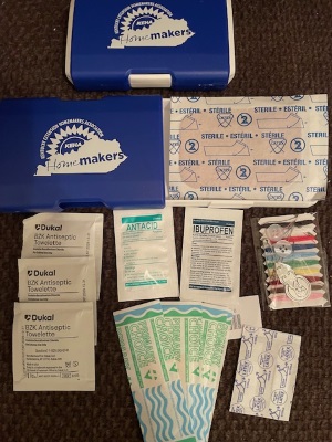 A blue and white box with the Kentucky Extensino Homemaker associate logo on it containing first aid items (badages, antiseptic towlettes, antaid, ibuprofen and a sewing kit with needles and thread.
